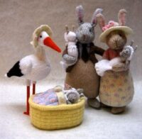 knitted toys of a stork delivering a bunny baby to a bunny couple