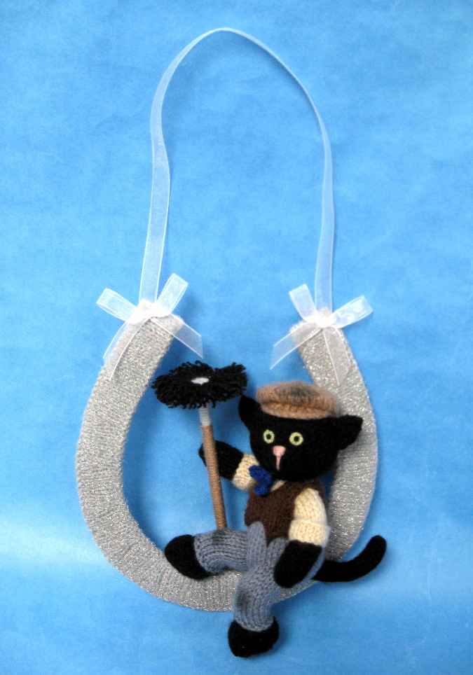 knitted toy of a black cat dressed as a chimney sweep sat in a horseshoe