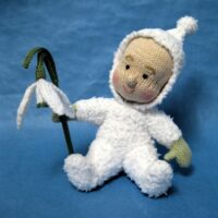 knitted toy of a baby dressed in white holding a large snowdrop