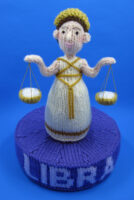 knitted toy of woman holding scales with Libra written below