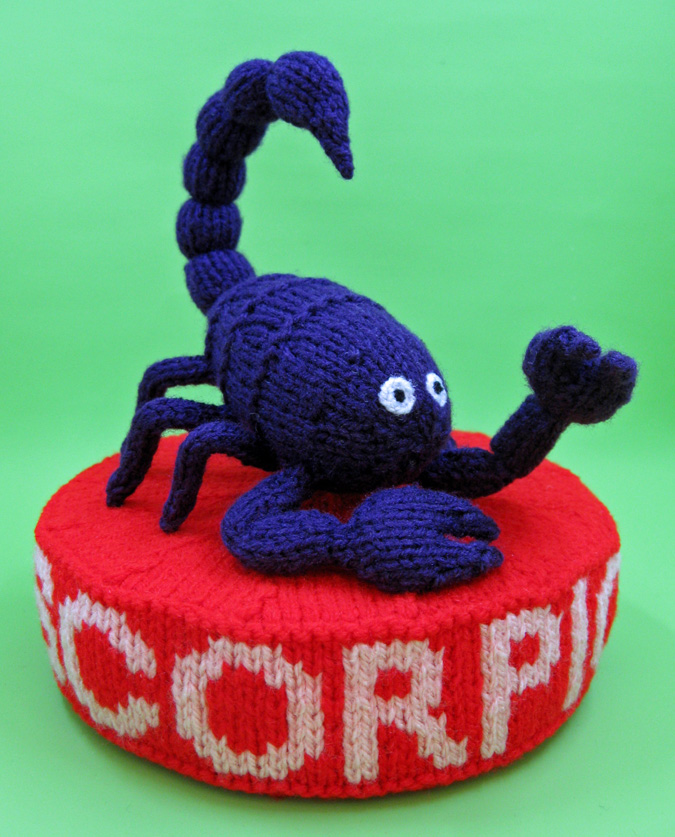 knitted toy of scorpion on plinth labelled scorpio