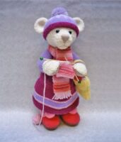 teddy knitted toy wearing a wooly hat and knitting a scarf